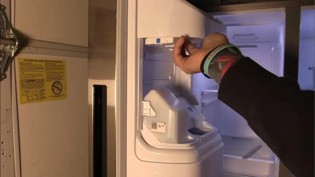 Hand removing ice maker from Samsung refrigerator inside the freezer compartment.